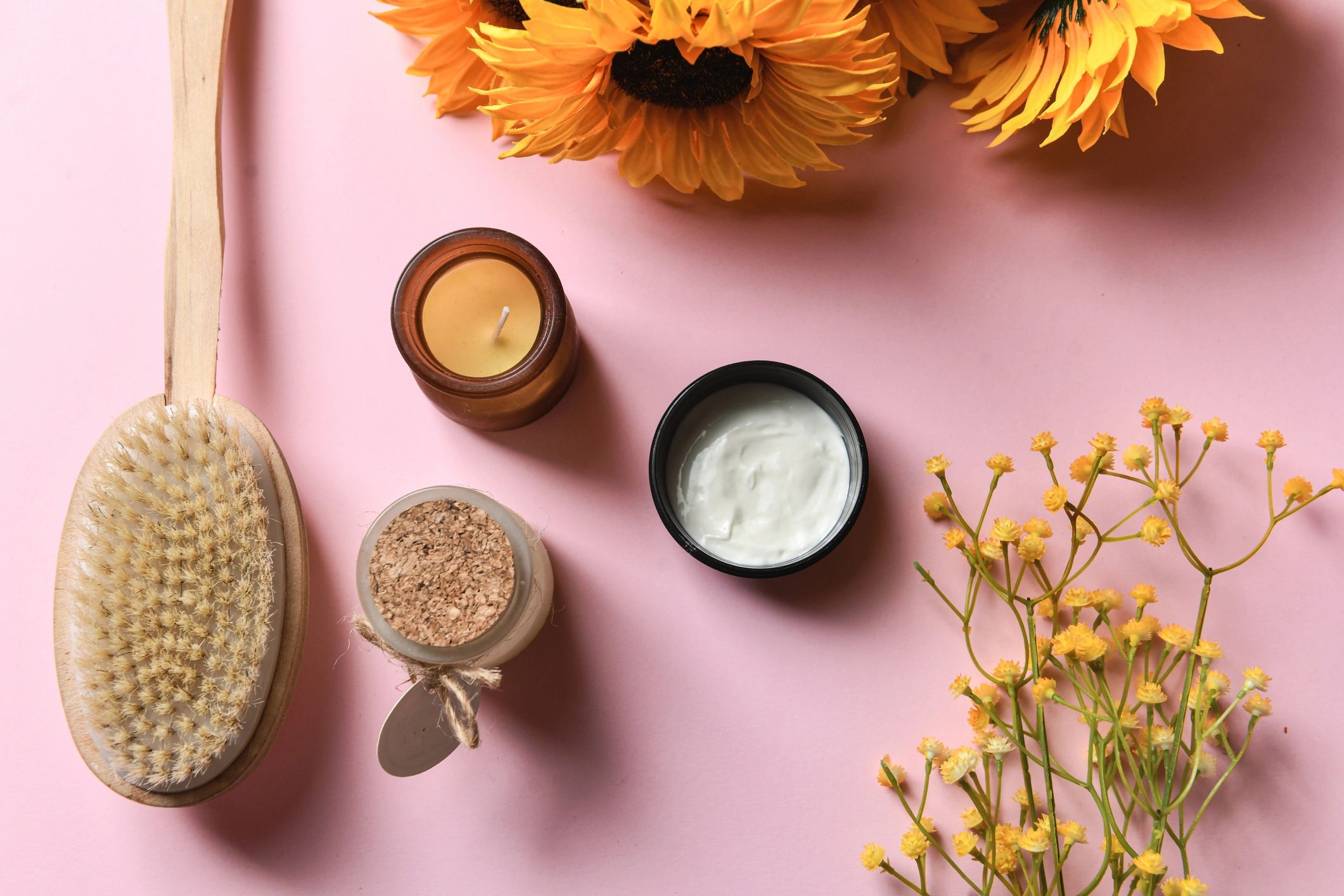 Flat lay of handmade soy candles and self-care items on a pink background