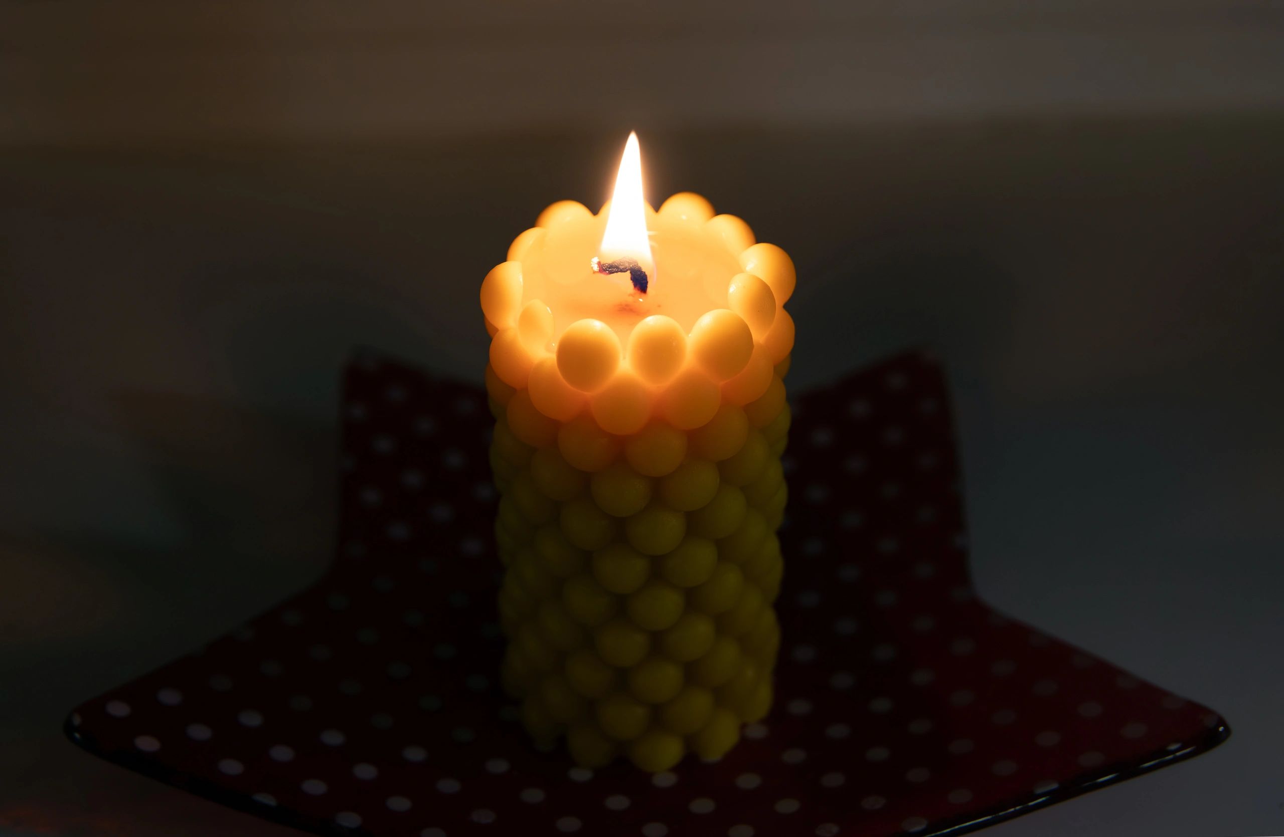 Bubbly-shaped beeswax candle burning on a windowsill